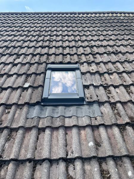 Finished grey-framed roof window with a pleated apron flashing over the tiles below