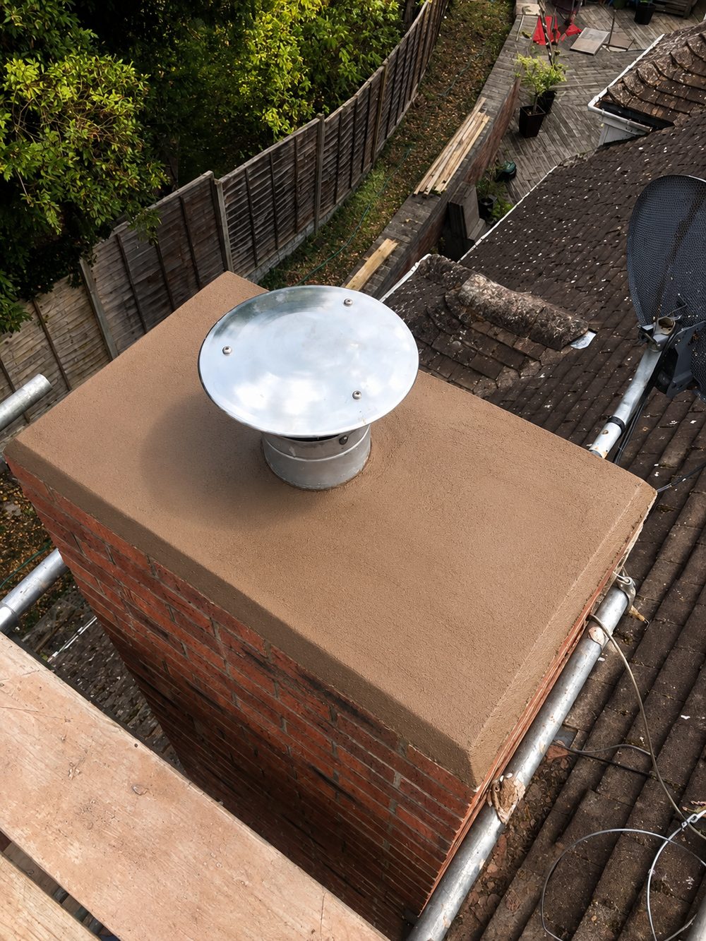 The top of a stack finished in fresh mortar to a fall, with a metal cowl standing over the closed flue opening