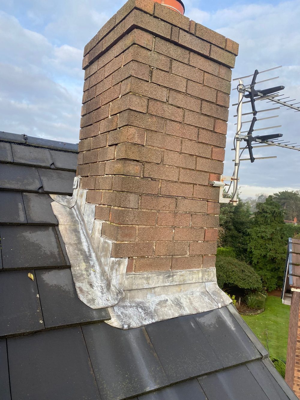 New lead at the base of a stack — a front apron across the downhill face and a stepped flashing dressed down the side