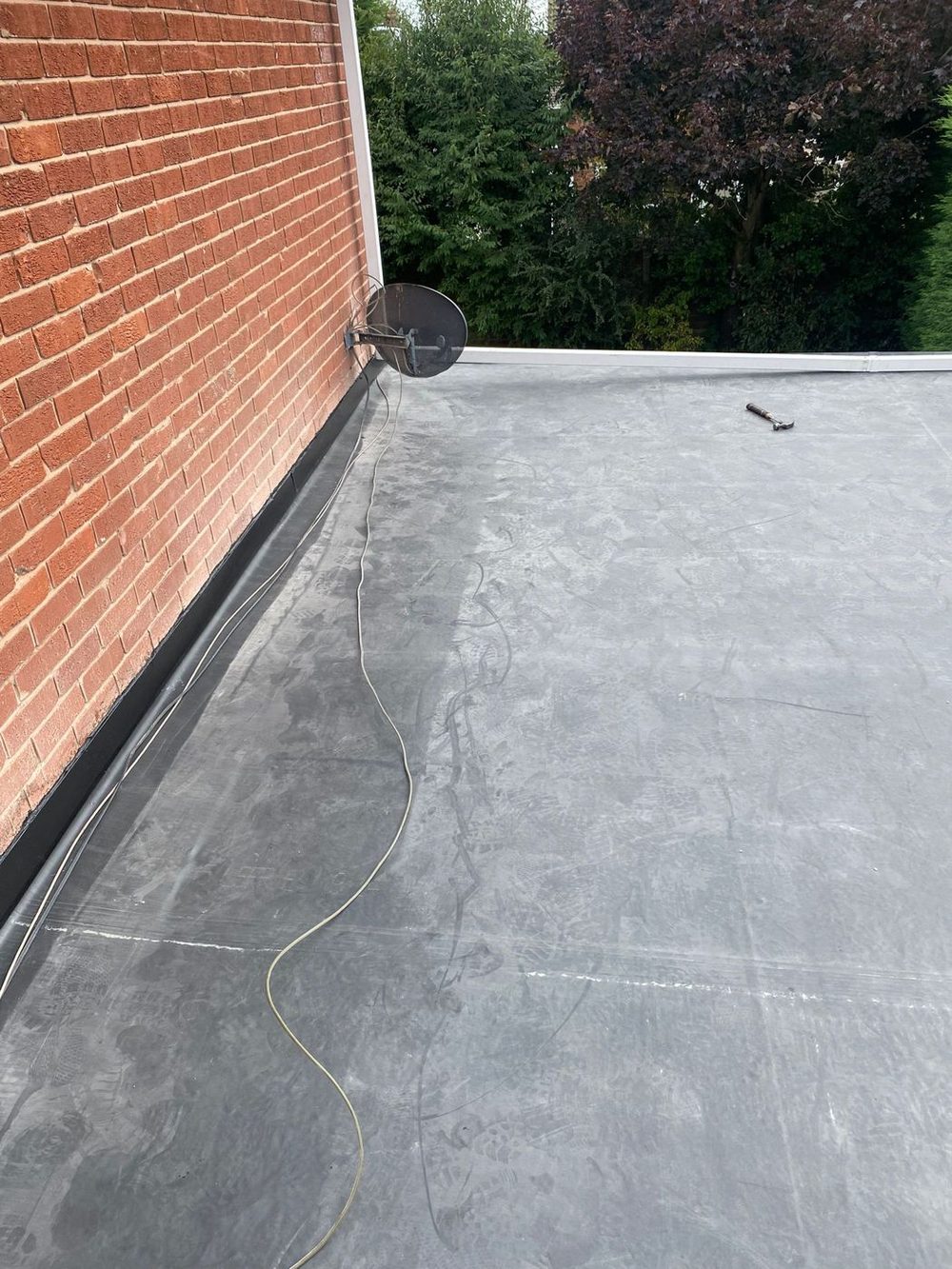 A finished EPDM roof taken up as an upstand against the house wall, with the trim run along the open edge