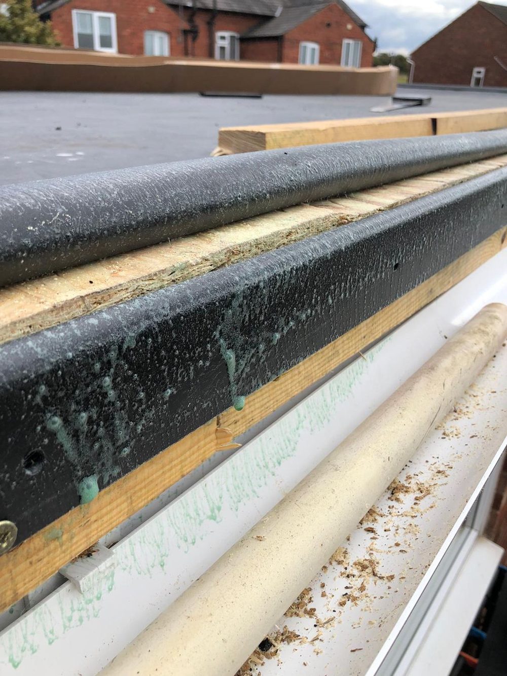A close-up of the edge trim — the membrane bonded over it and the adhesive line along the timber below