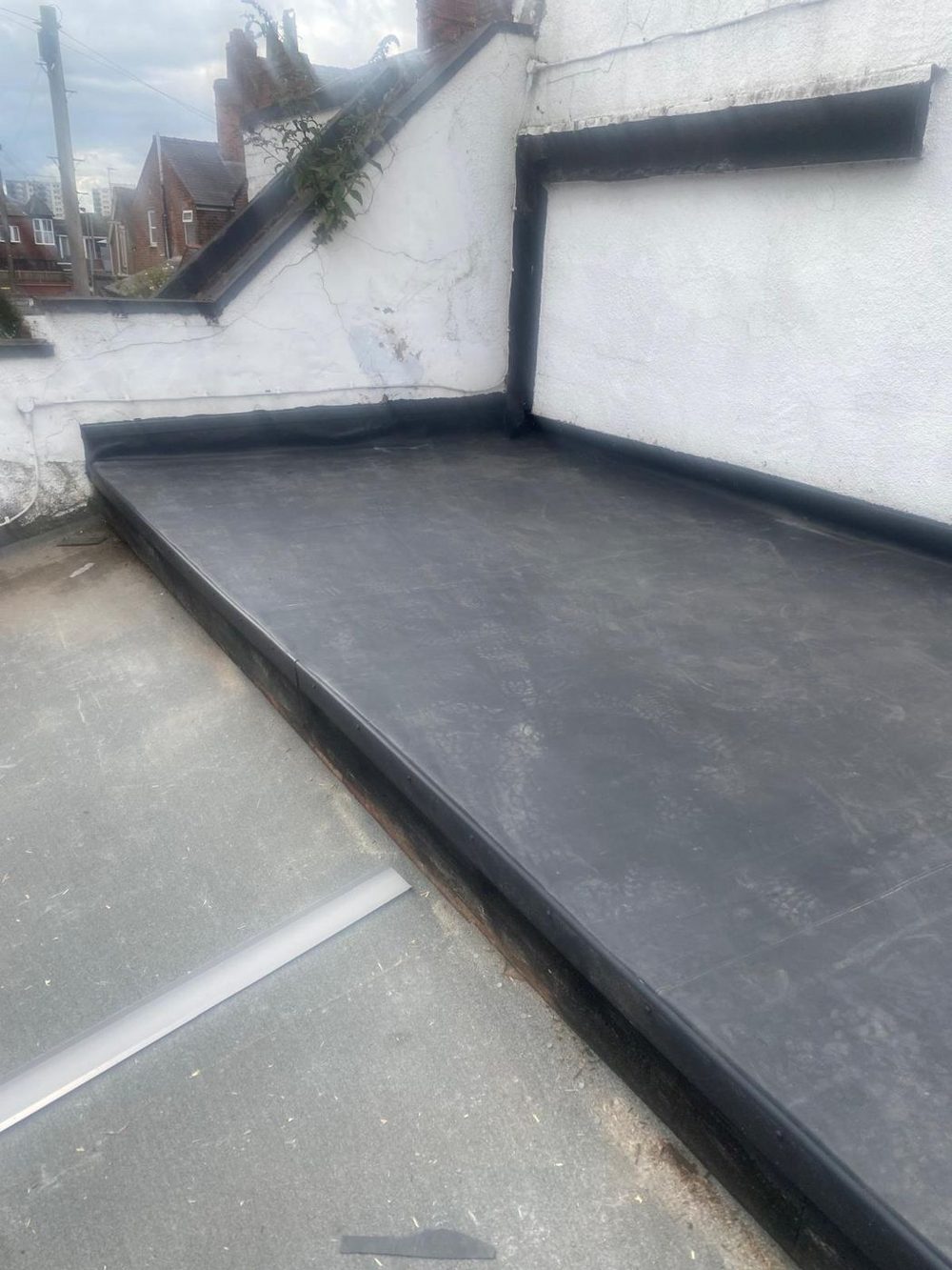 The covering carried up a rendered wall as an upstand and returned round the corner, a lower roof beyond