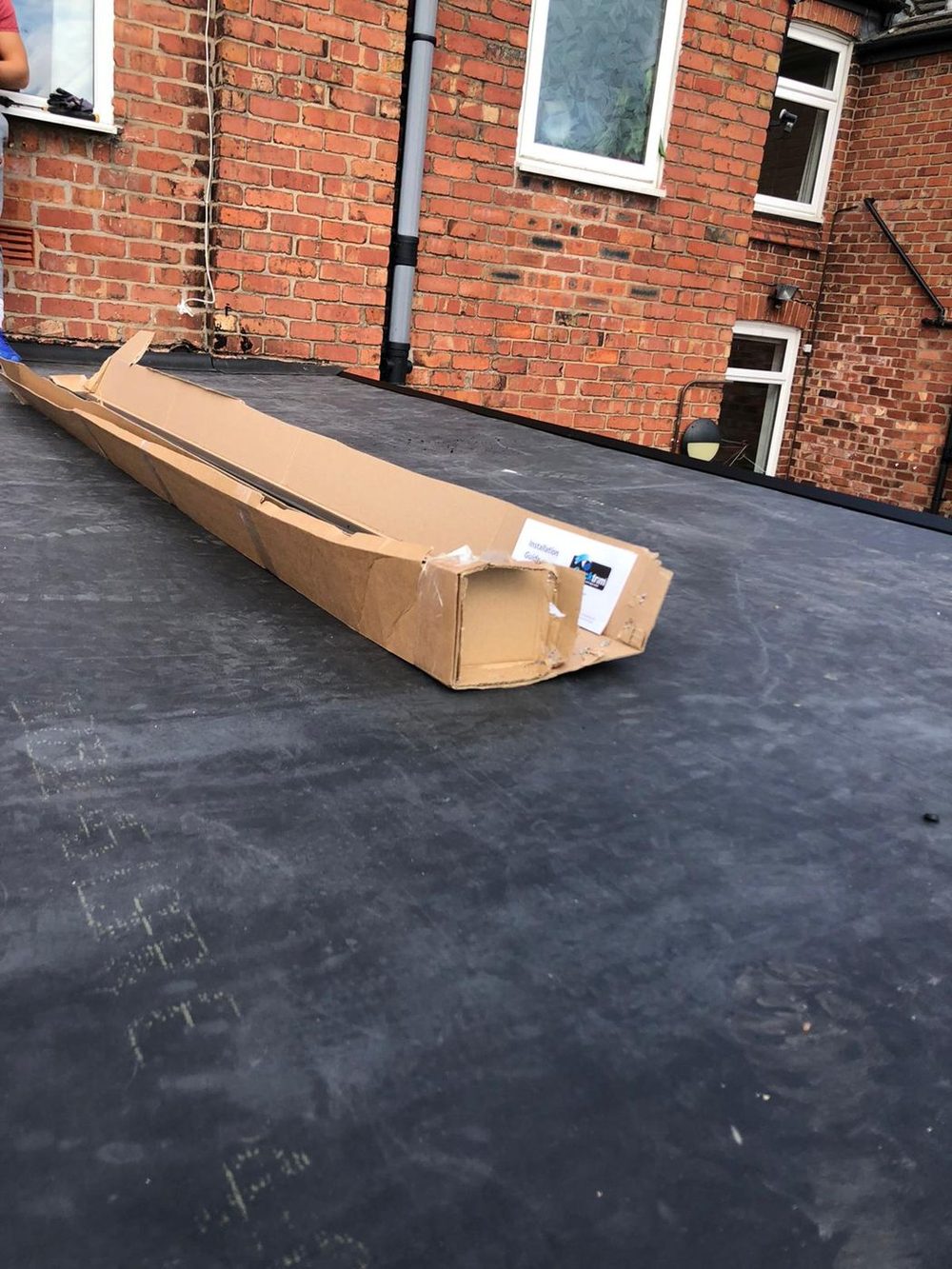 A large rear flat roof with the sheet down and turned up against the house wall, a long boxed delivery lying on it