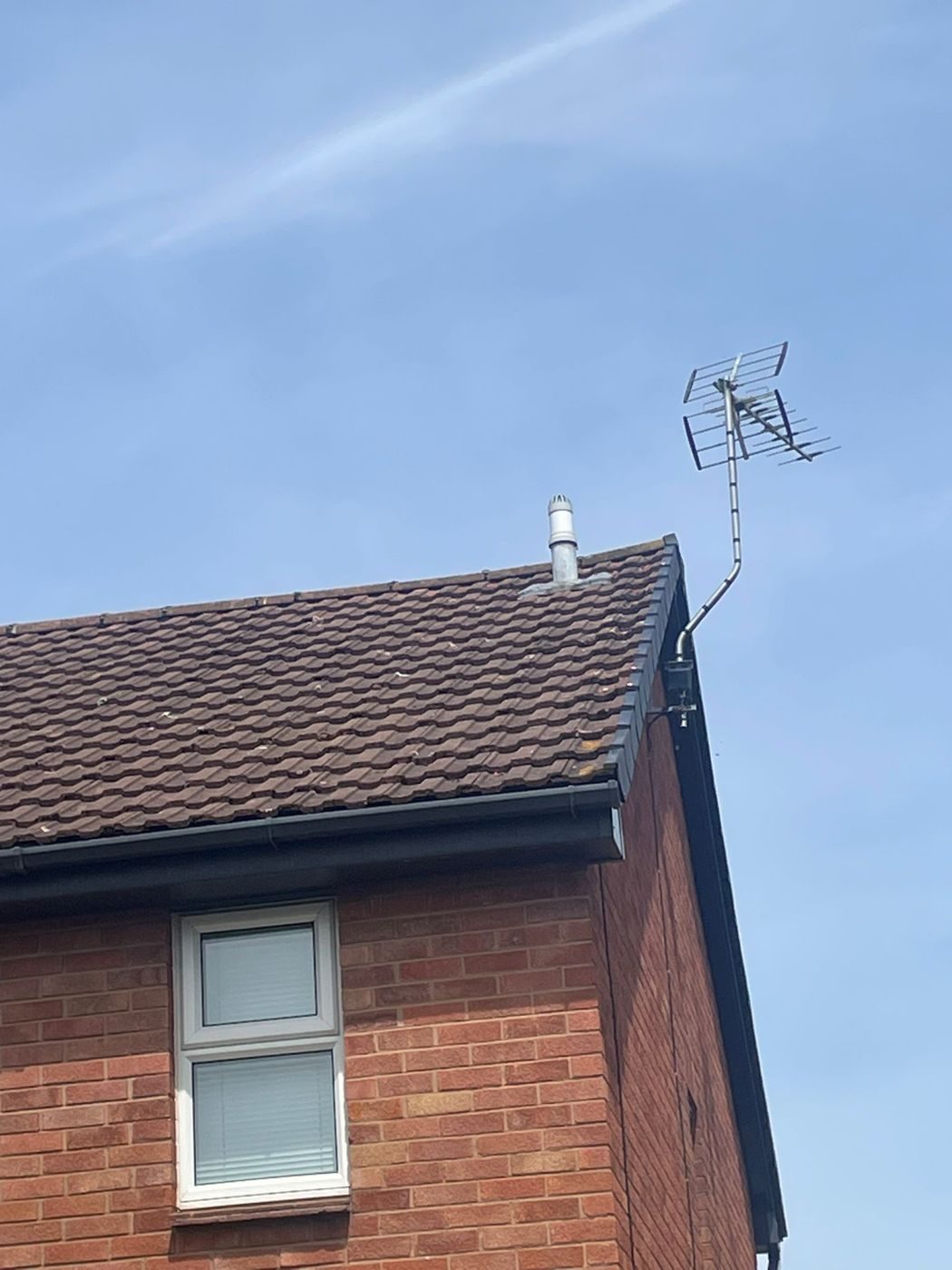 The gable corner of a tiled roof with the verge trim run over the edge, black fascia and gutter below