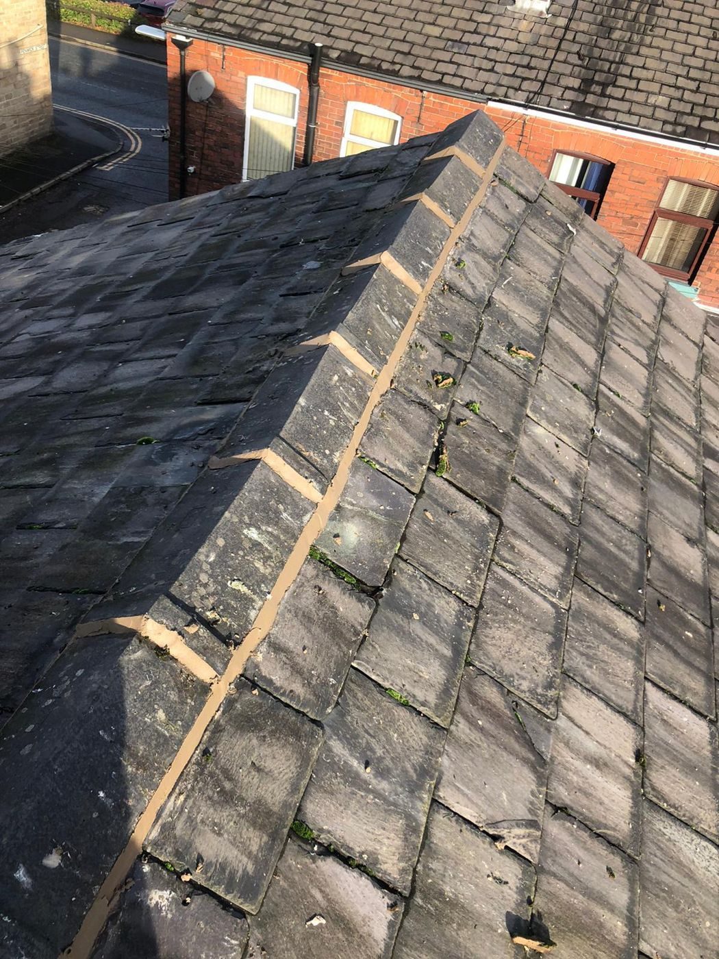 Mortar bedding set out in dabs along a stripped hip on a weathered slate roof, before the hip tiles and their fixings go on