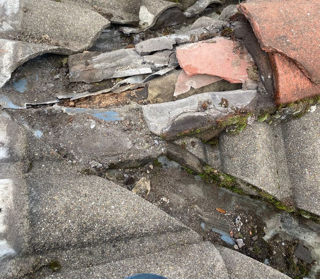 Broken tiles, crushed slate packing and decayed mortar at a failed roof junction, with split lead beneath