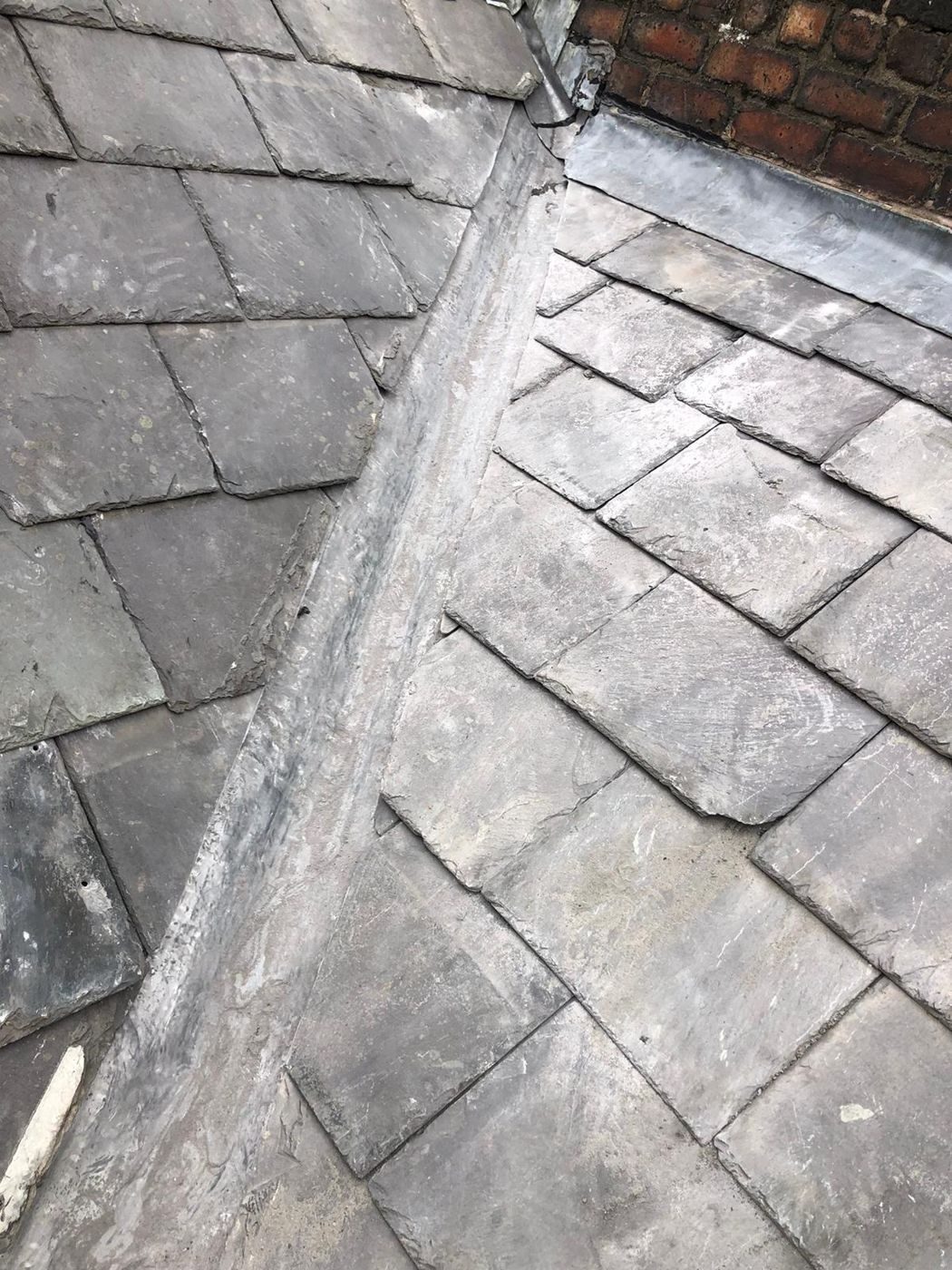 The completed lead valley between natural slates, meeting lead flashing against a red brick wall at the head