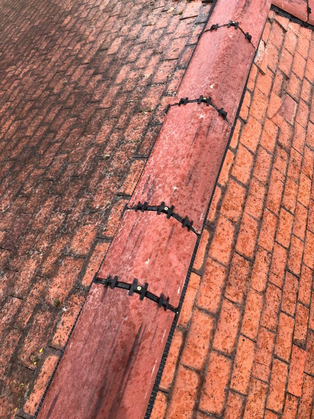 Ridge tiles seated on a dry ridge roll, every joint held down by a black mechanical clip rather than mortar alone