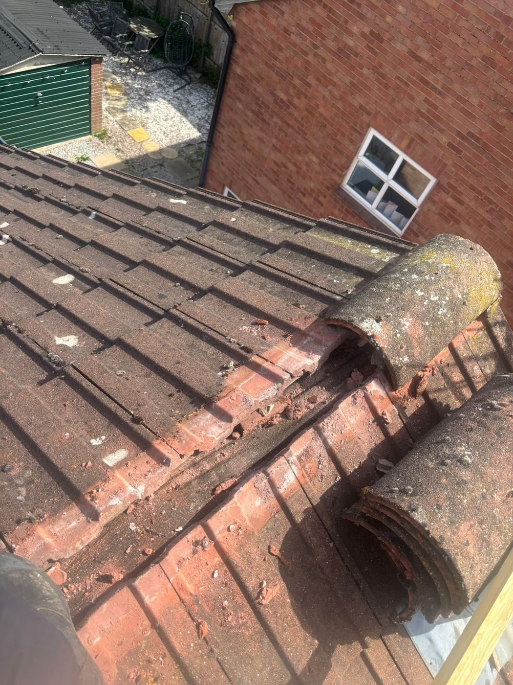 Two weathered half-round ridge tiles lifted clear of crumbling mortar bedding on a brown tiled roof