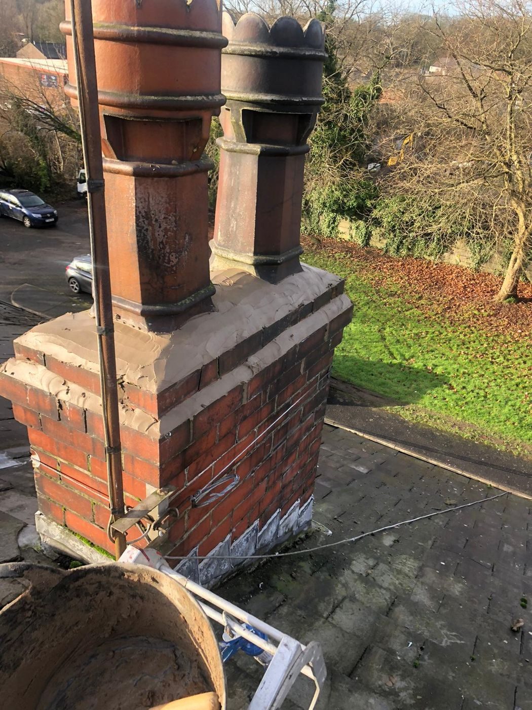 A repointed brick chimney stack with fresh flaunching and a row of tall clay pots, terracotta and dark-glazed, standing on a slate roof