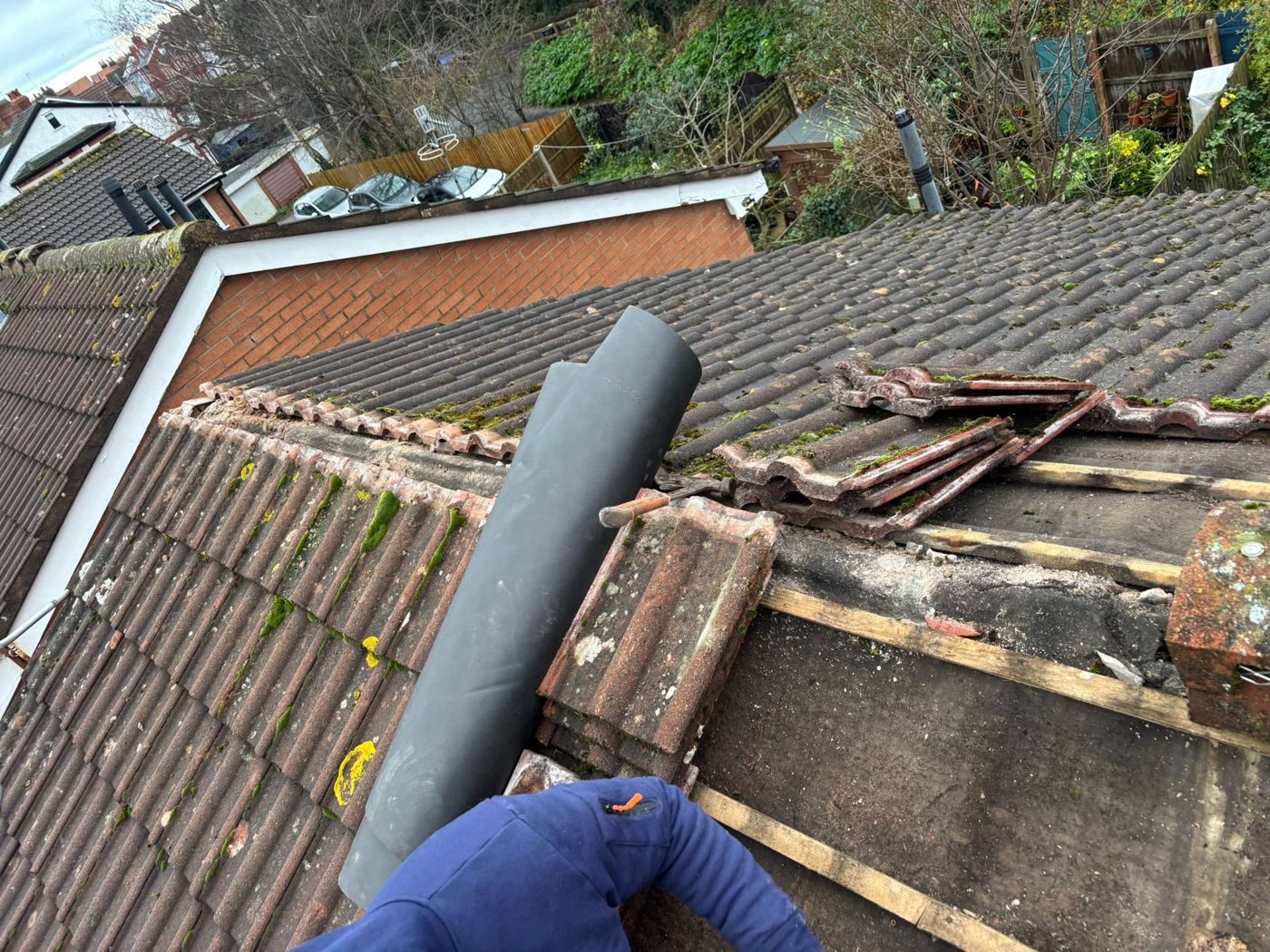 A roll of underlay being laid across a stripped section of tiled roof, the old tiles stacked on the exposed battens