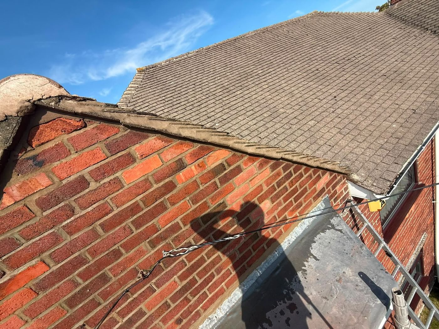Cracked mortar verge along a tiled gable above red brickwork, blown away from the tile at the apex