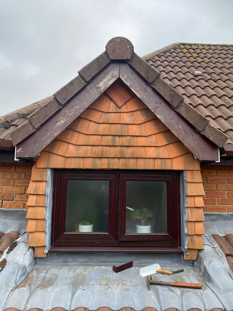 The dormer on the Runcorn job seen from the roof, with rosewood bargeboards mitred at the apex over cedar shingle cheeks, a lead apron beneath the window and hand tools resting on the lead